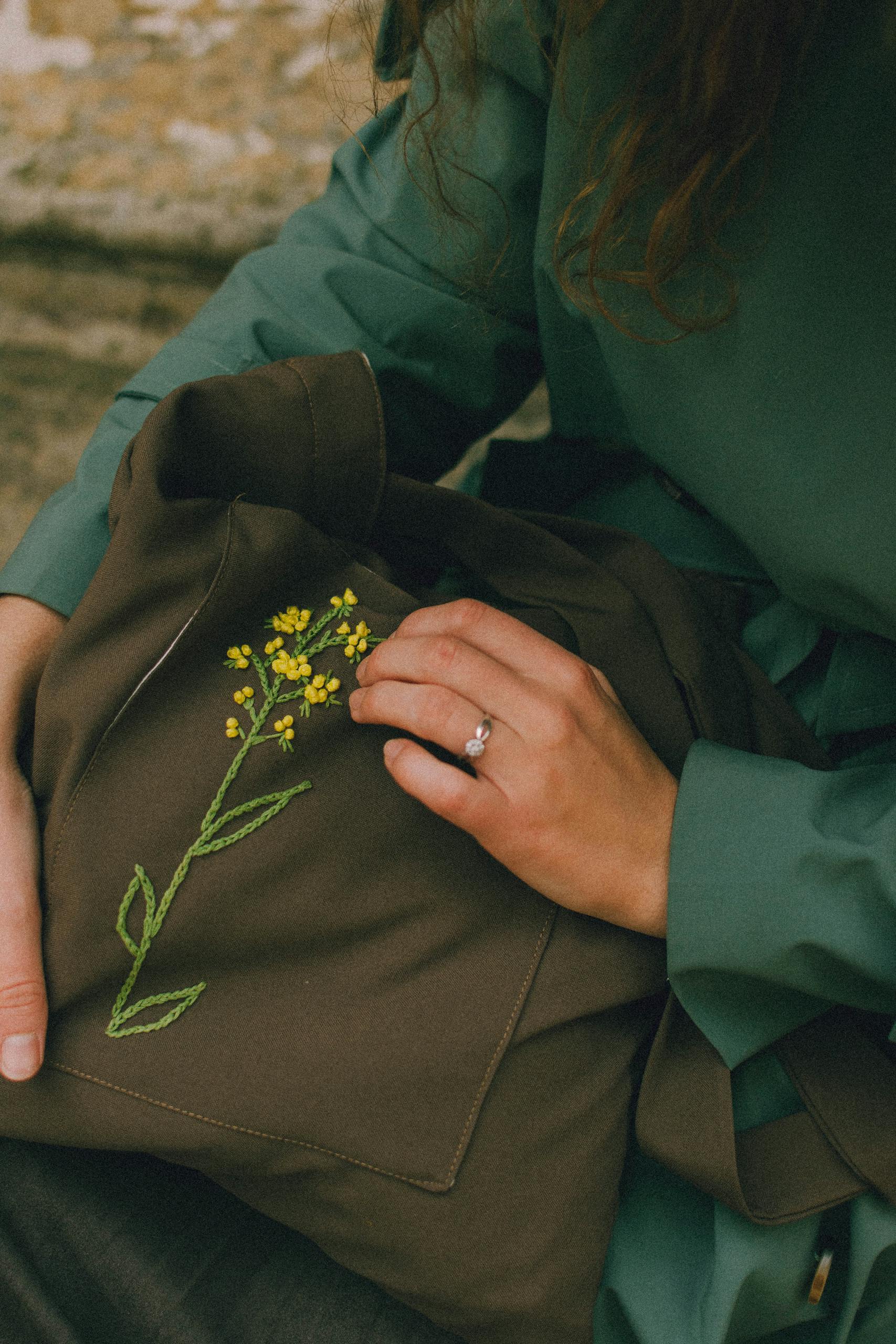 Womans hands holding olive colour textile bag with embroidered yellow flower